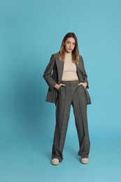 Photo of Full length portrait of beautiful young woman in fashionable suit on light blue background. Business attire