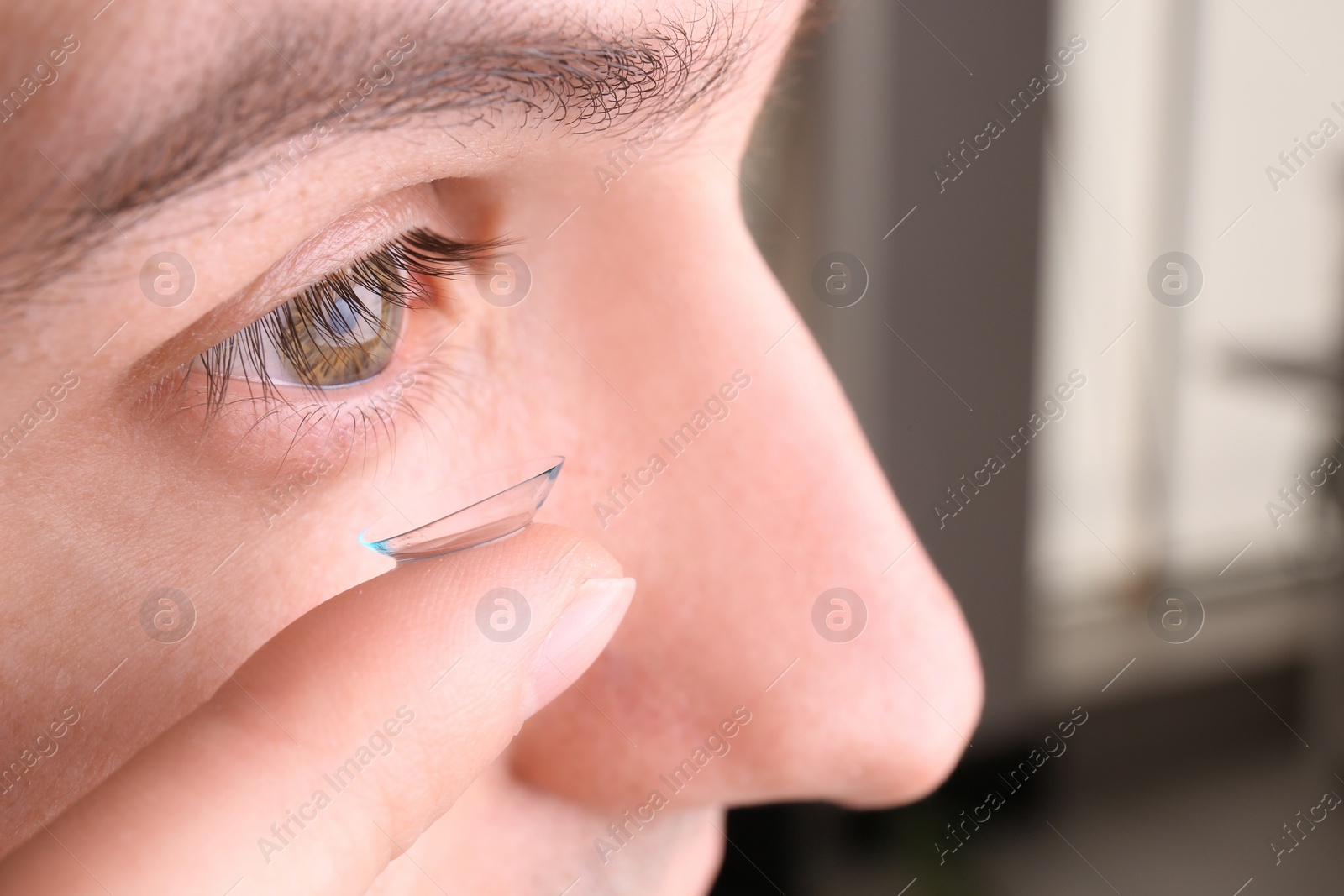 Photo of Young man putting contact lens in his eye, closeup