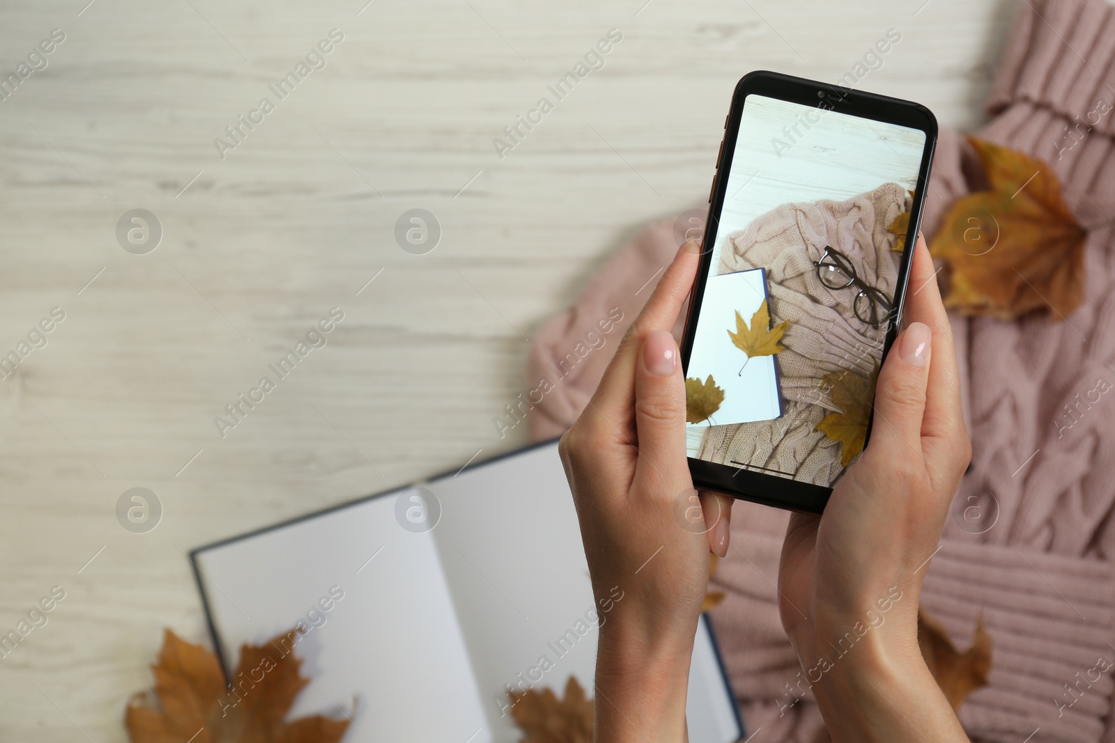 Photo of Woman taking photo of autumn composition with smartphone at beige wooden table, top view. Space for text