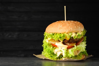 Photo of Burger with delicious patty on gray table against dark background, space for text