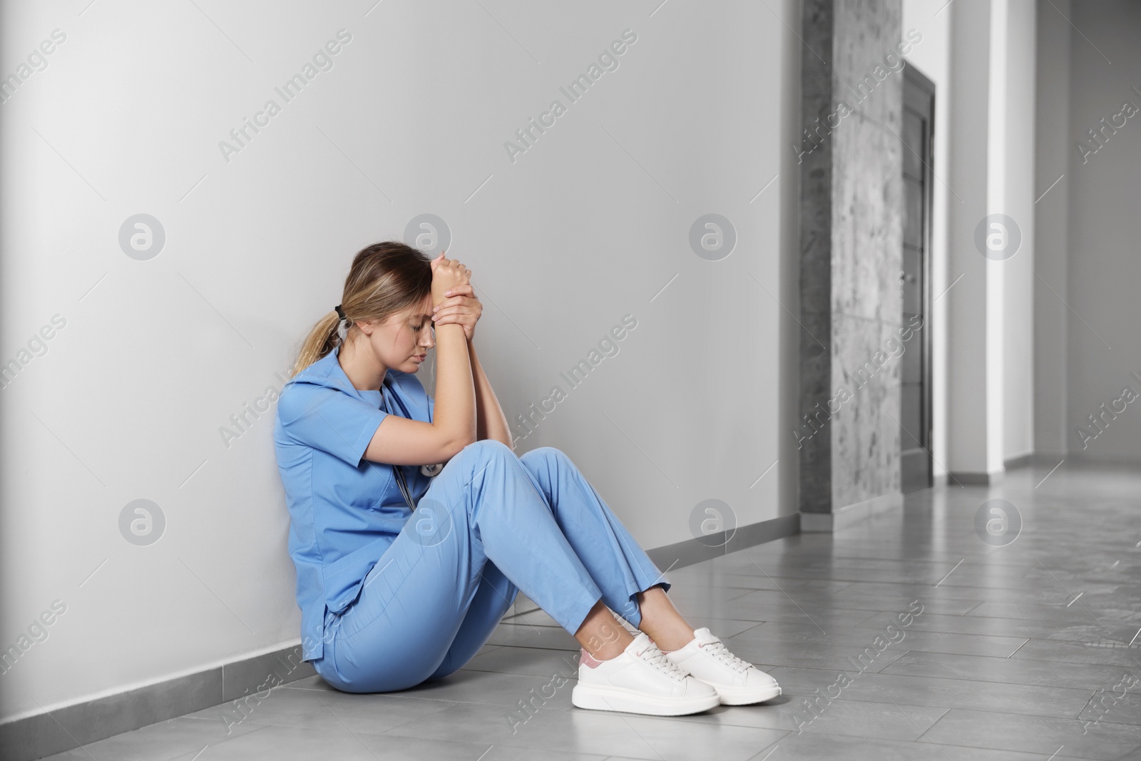 Photo of Exhausted doctor sitting on floor in hospital, space for text