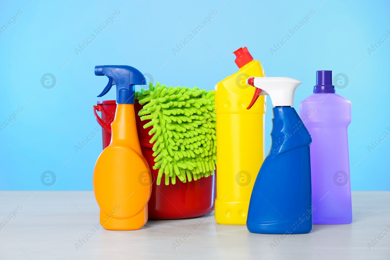 Photo of Bucket with different cleaning products and supplies on light table