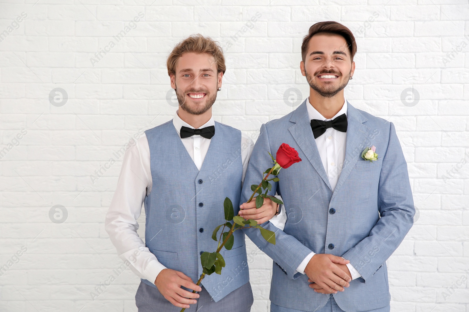 Photo of Happy newlywed gay couple with flower against white wall