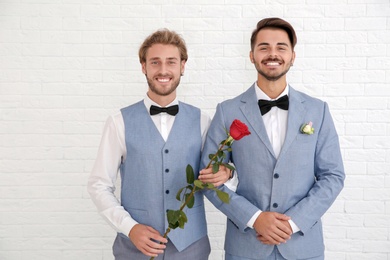 Happy newlywed gay couple with flower against white wall