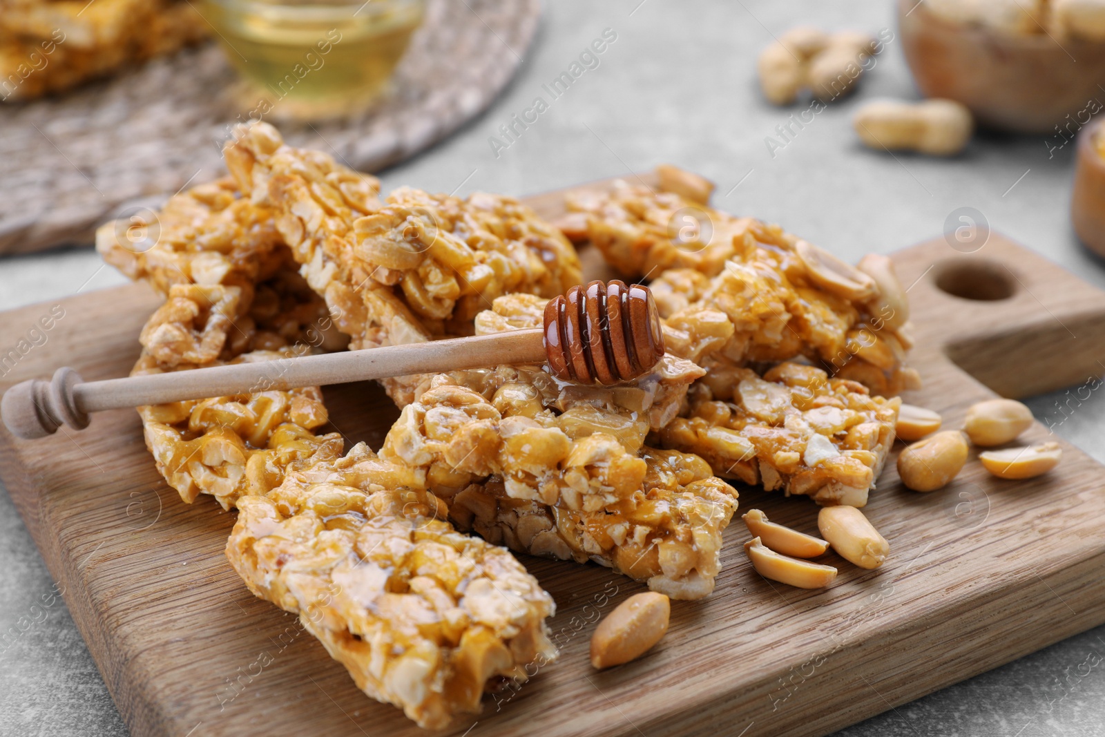 Photo of Delicious peanut kozinaki bars and honey dipper on wooden board, closeup