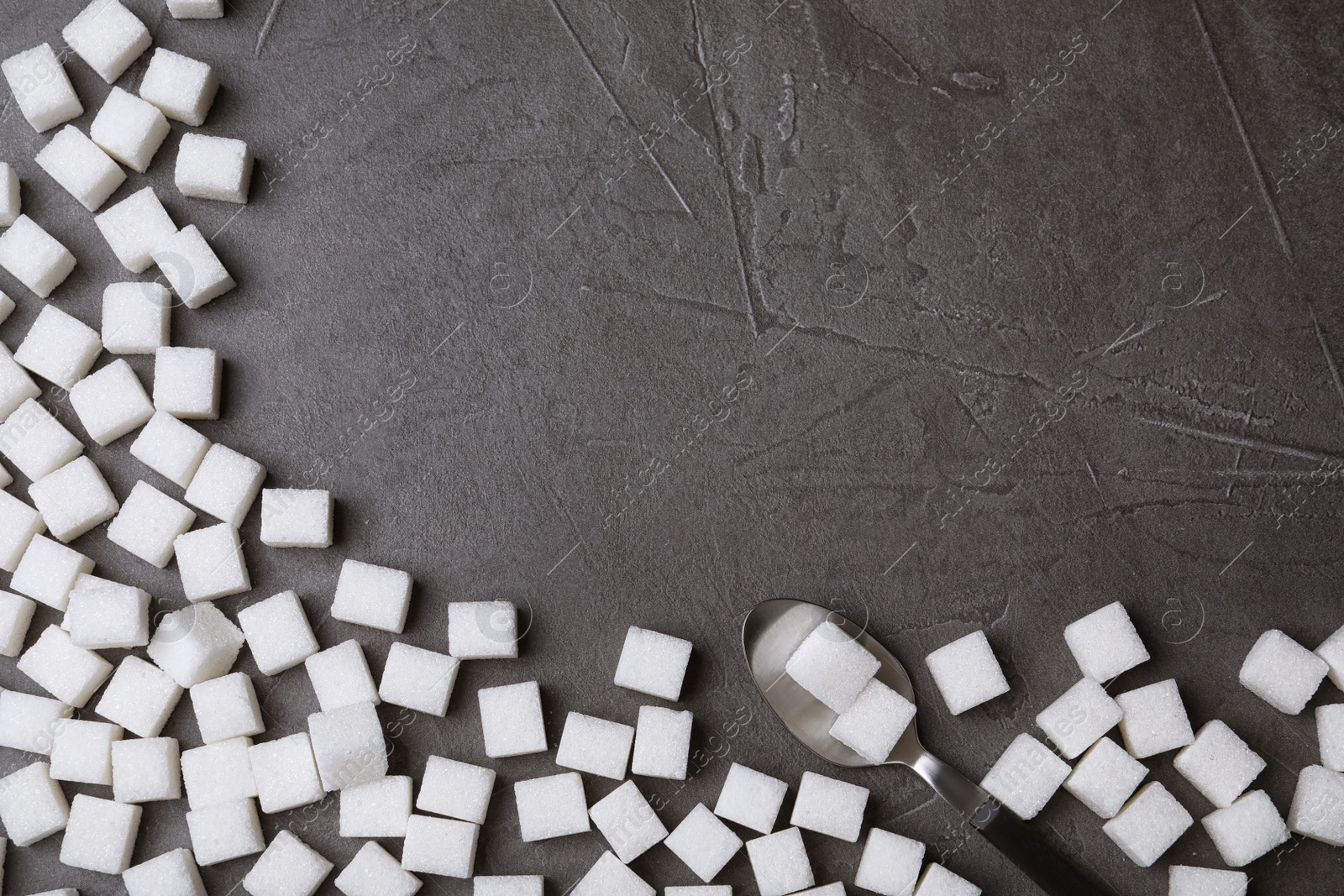 Photo of Refined sugar cubes and spoon on black table, top view. Space for text