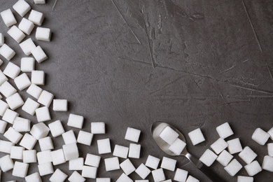 Photo of Refined sugar cubes and spoon on black table, top view. Space for text