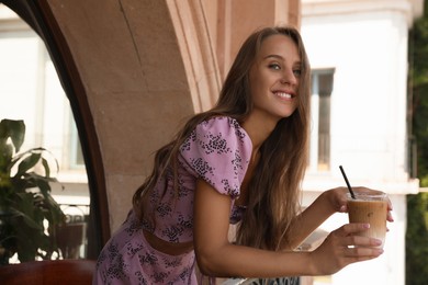 Photo of Beautiful young woman with glass of coffee standing on balcony