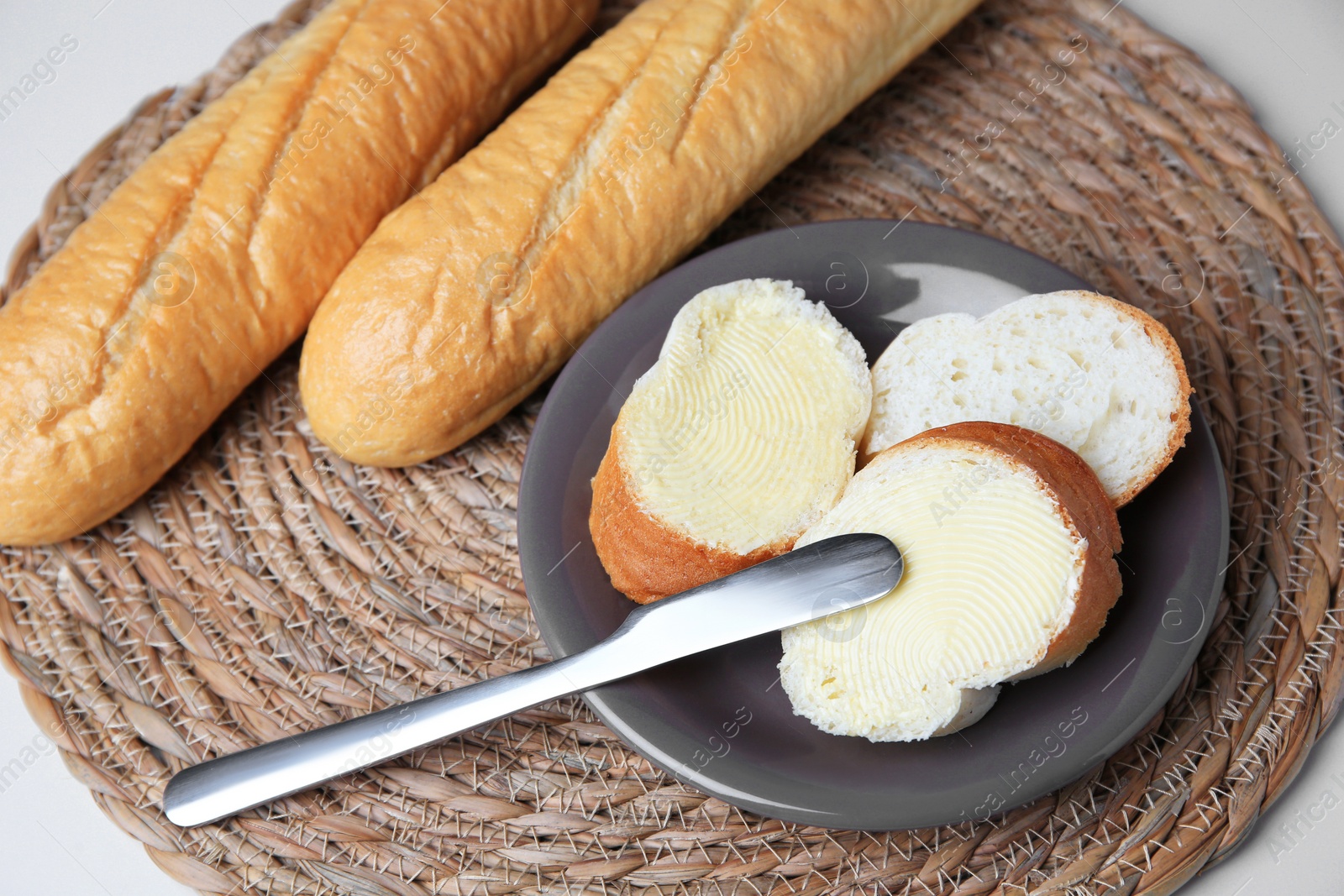 Photo of Whole and cut baguettes with fresh butter on white table, above view