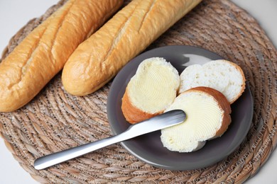 Photo of Whole and cut baguettes with fresh butter on white table, above view