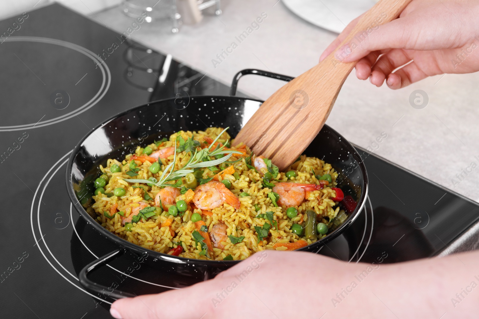 Photo of Woman cooking tasty rice with shrimps and vegetables on induction stove, closeup