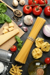 Different types of pasta, spices, garter and products on dark textured table, flat lay