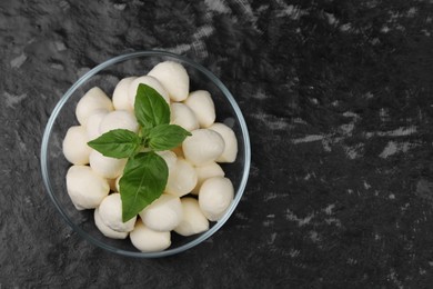 Tasty mozzarella balls and basil leaves in bowl on black textured table, top view. Space for text