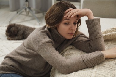 Photo of Sad young woman sitting near sofa at home