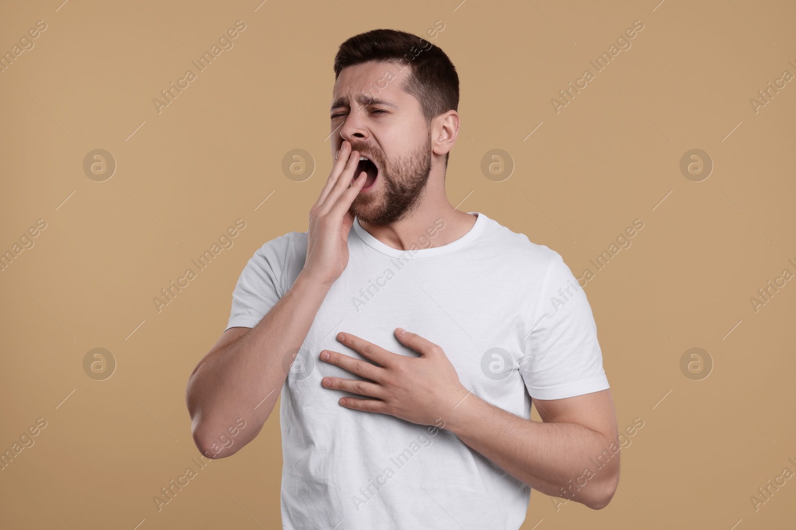 Photo of Sleepy man yawning on beige background. Insomnia problem