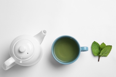 Cup with hot tea, mint and teapot on white background, top view