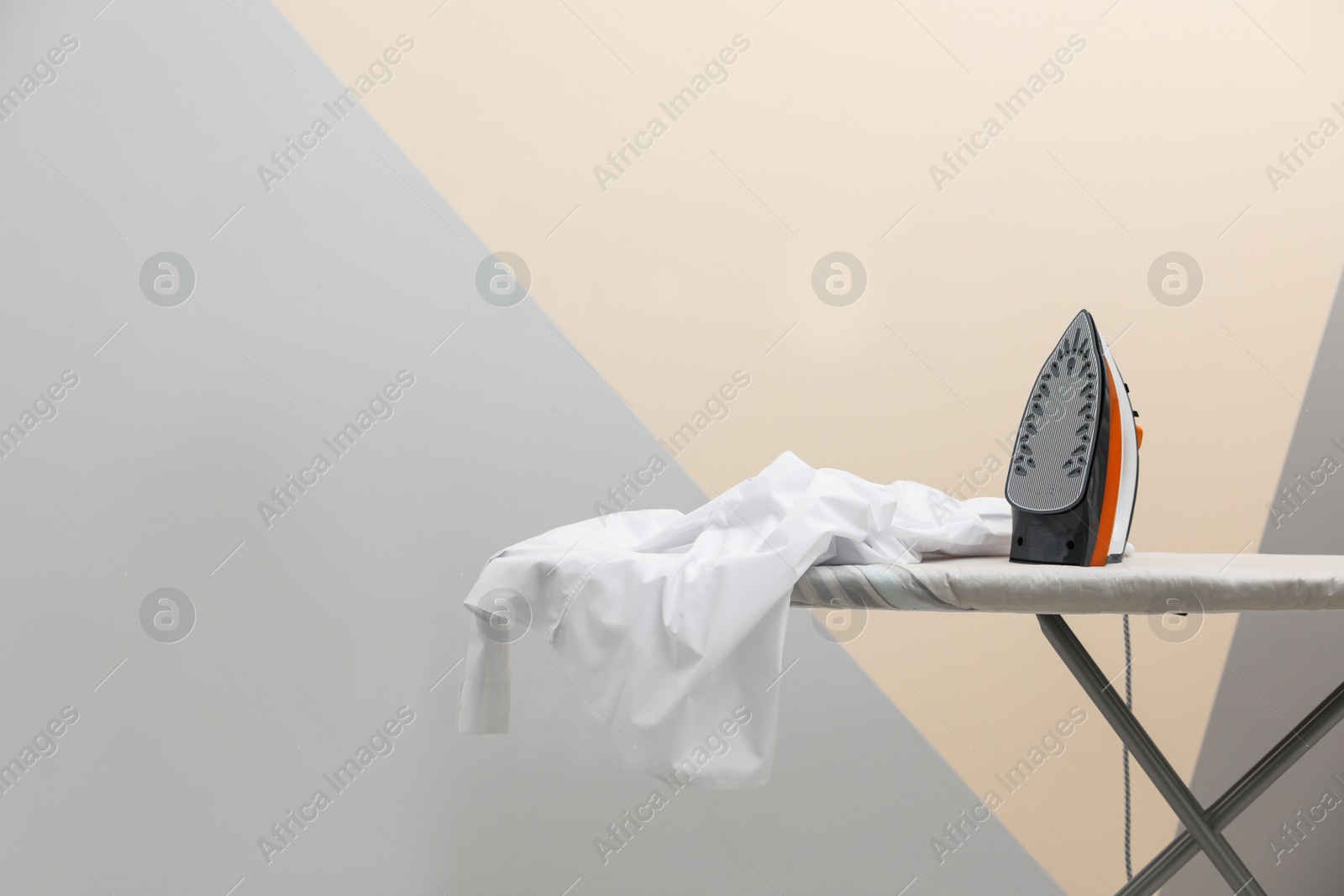 Photo of New modern iron and clean shirt on board against color background, space for text. Laundry day