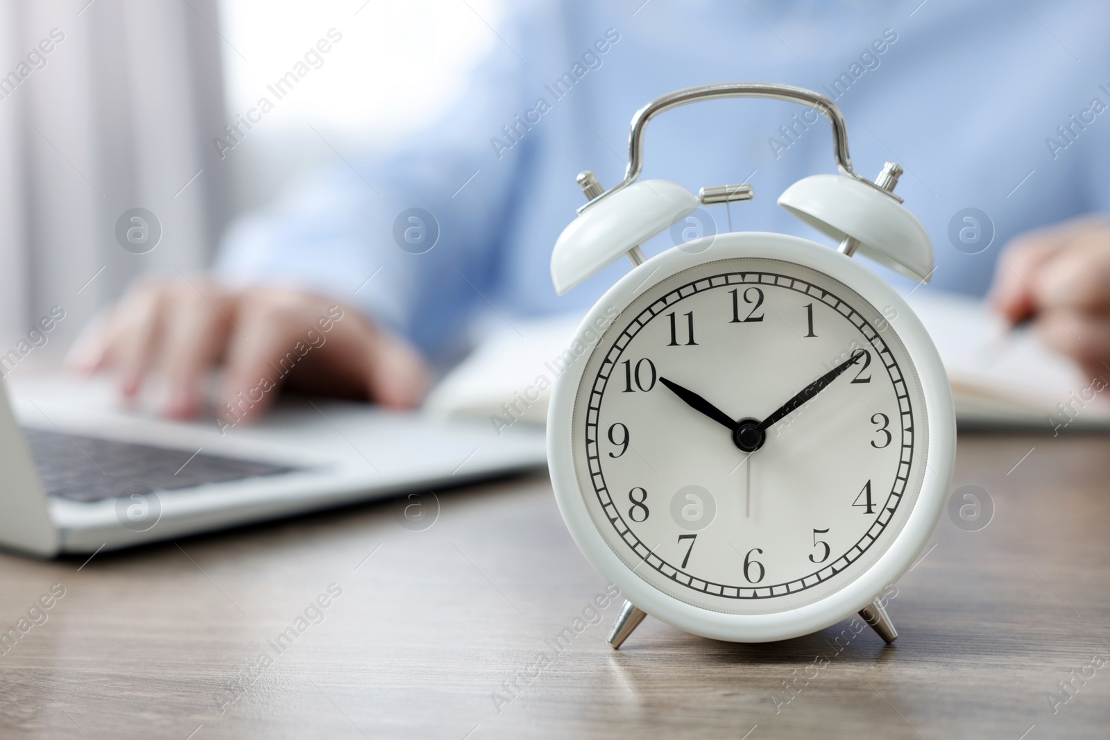 Photo of White alarm clock and man working at table, closeup. Space for text