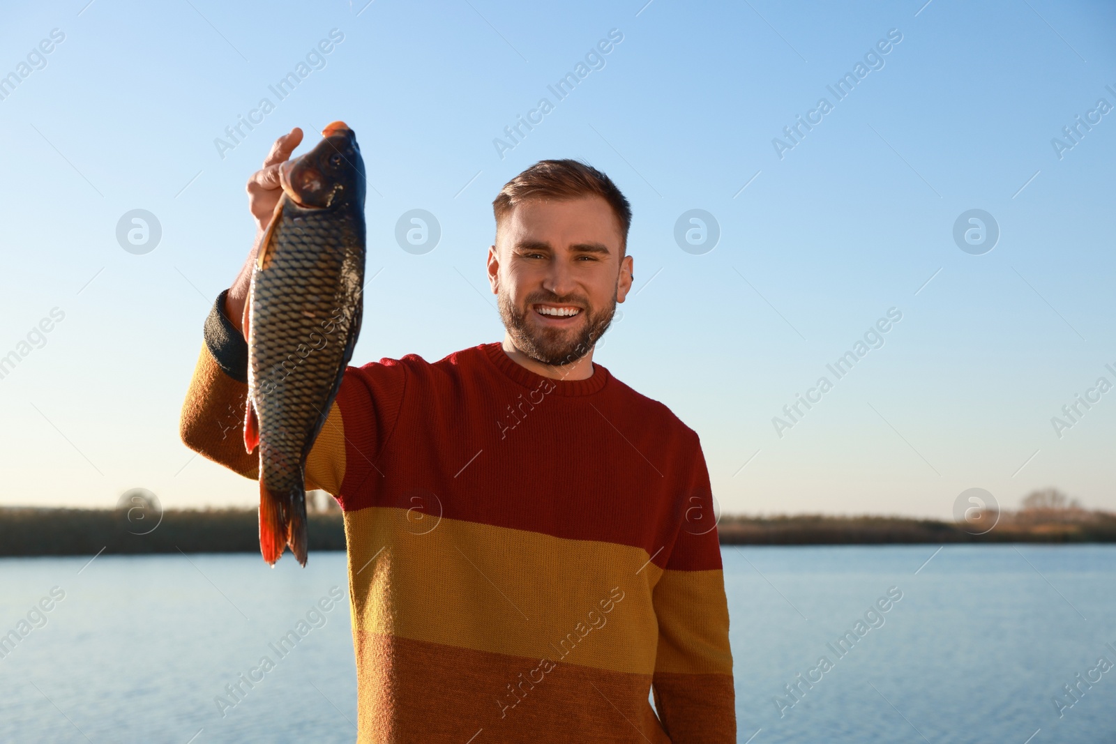 Photo of Fisherman holding caught fish at riverside. Recreational activity