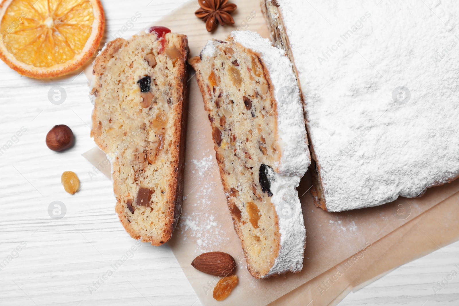 Photo of Traditional Christmas Stollen with icing sugar on white wooden table, flat lay