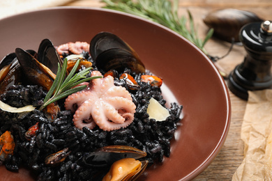 Photo of Delicious black risotto with seafood on wooden table, closeup