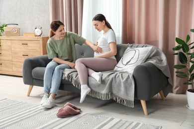 Doula taking care of pregnant woman on sofa at home. Preparation for child birth