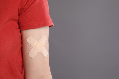 Woman with sticking plaster on her arm against grey background, closeup. Space for text