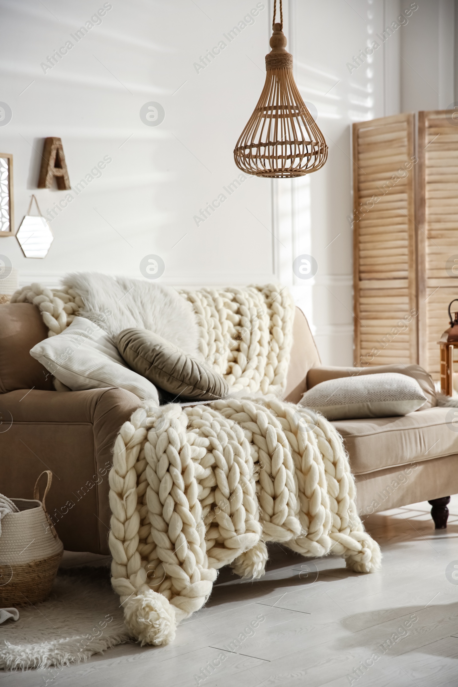 Photo of Cozy living room interior with beige sofa, knitted blanket and cushions