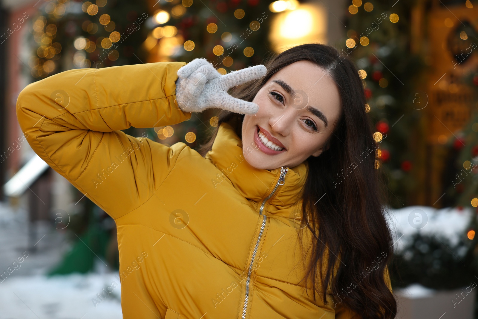 Photo of Portrait of smiling woman showing peace sign on city street in winter