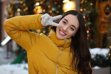 Portrait of smiling woman showing peace sign on city street in winter