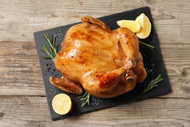 Photo of Tasty roasted chicken with spices and lemon on wooden table, top view