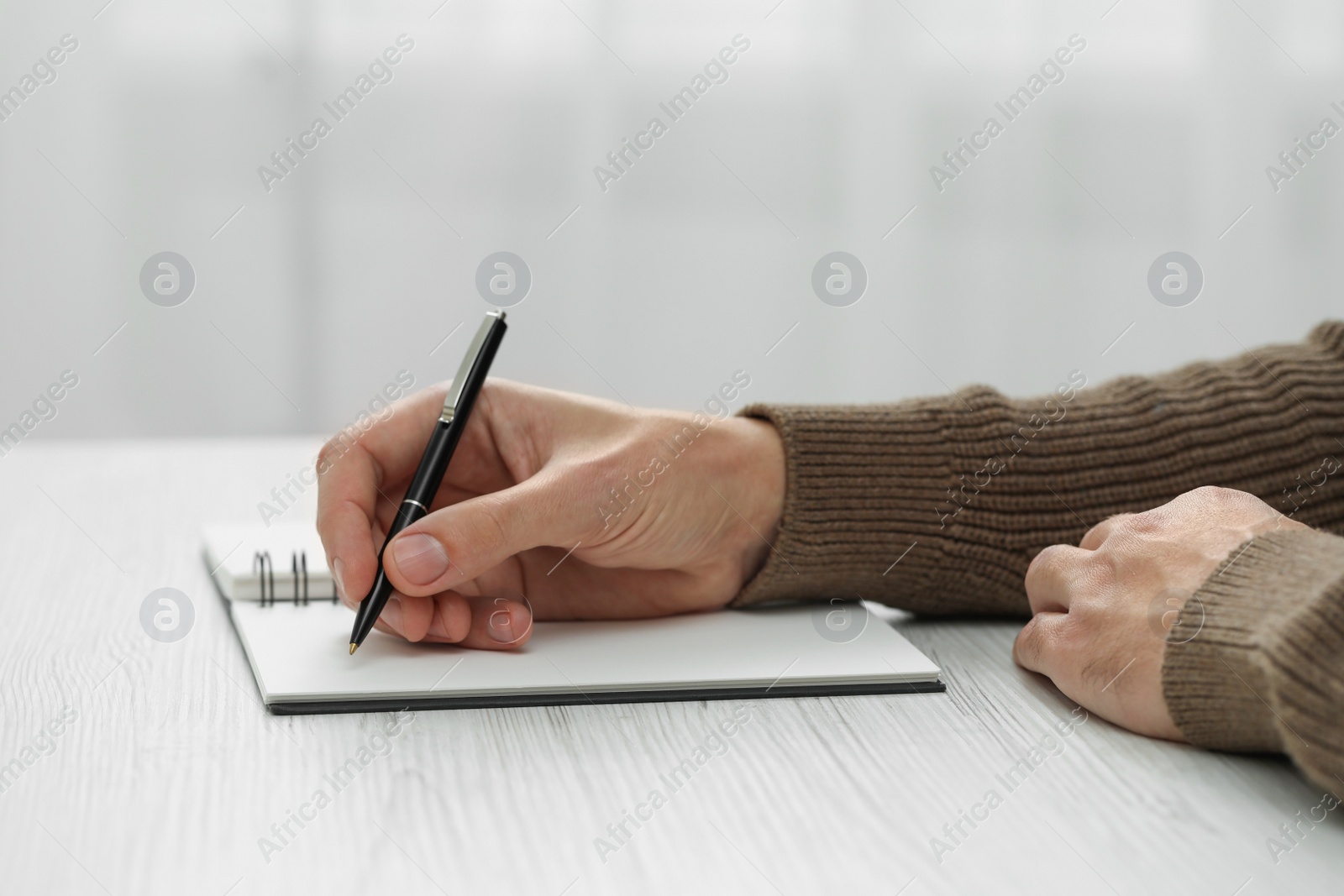 Photo of Man writing in notebook at white wooden table, closeup