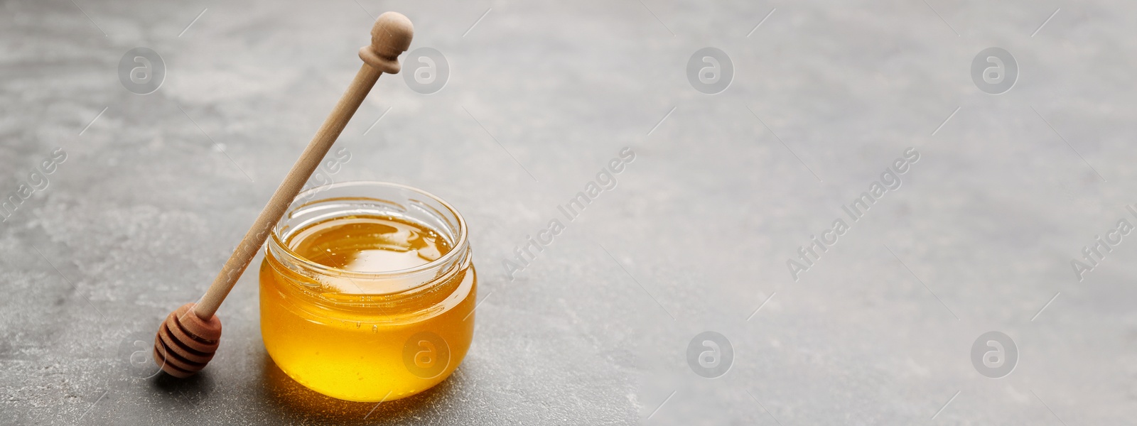 Image of Tasty honey and wooden dipper on light grey table, space for text. Banner design