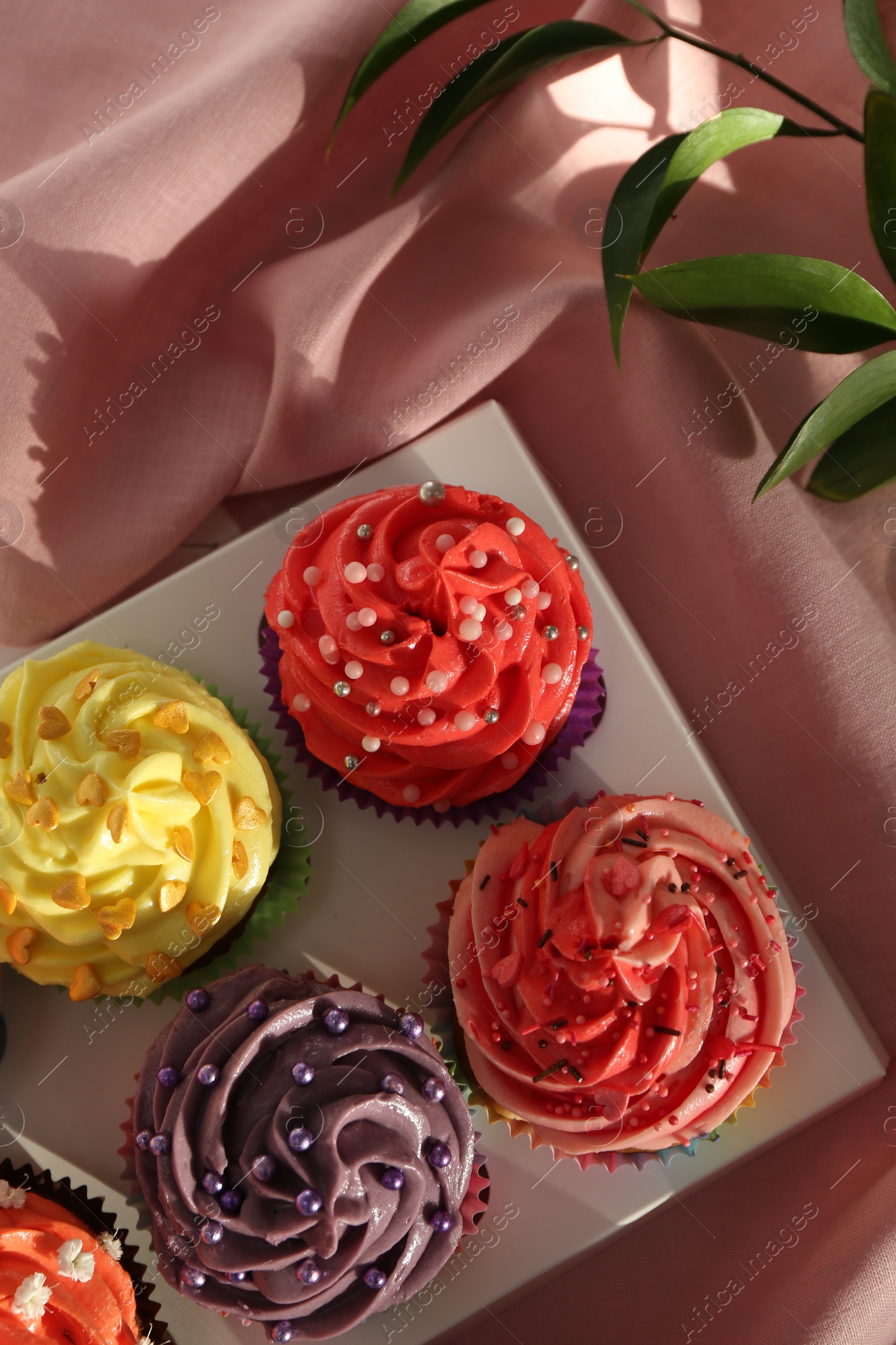 Photo of Delicious cupcake with bright cream on pink fabric, top view