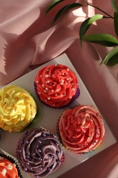 Delicious cupcake with bright cream on pink fabric, top view