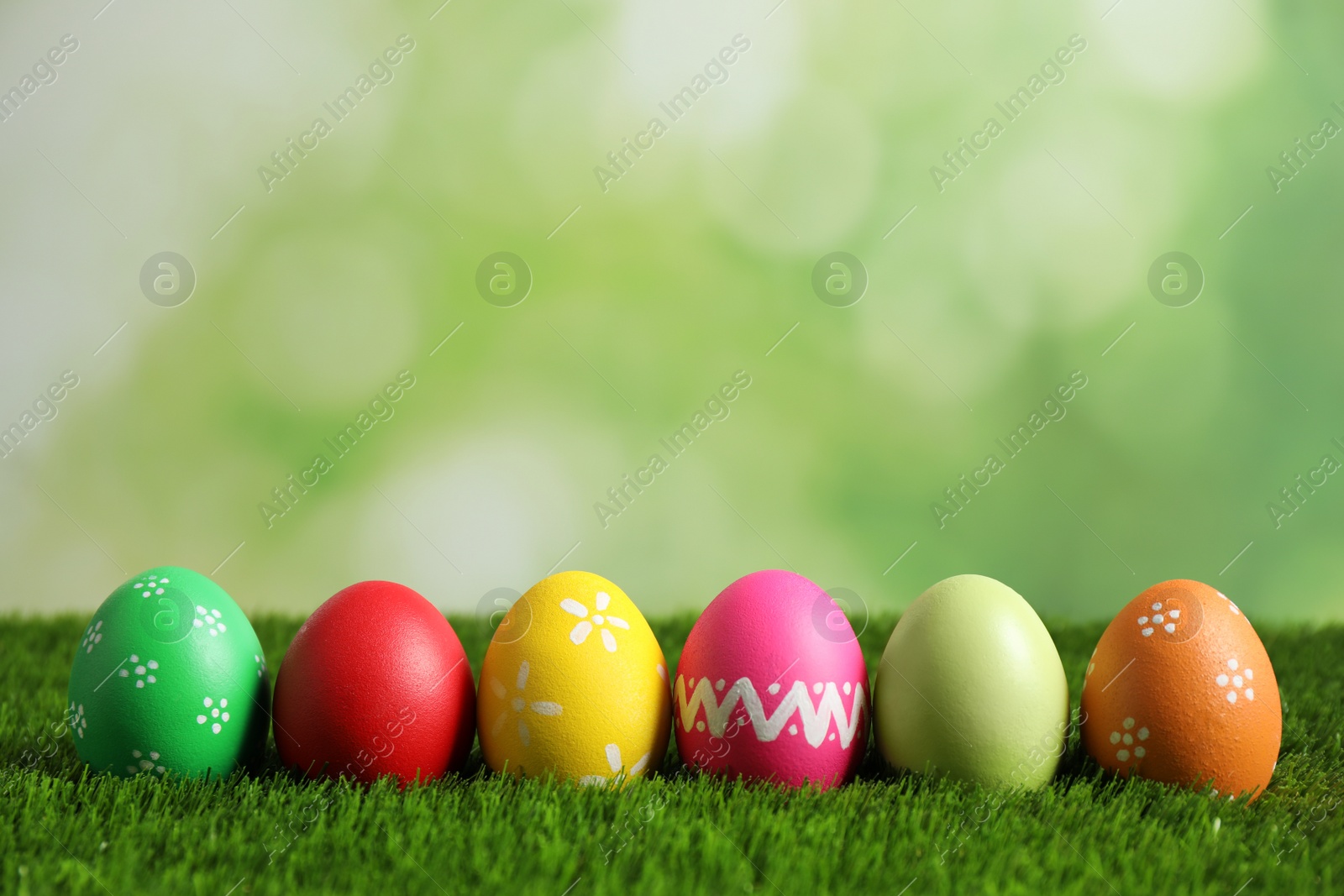 Photo of Colorful Easter eggs on green grass against blurred background. Space for text