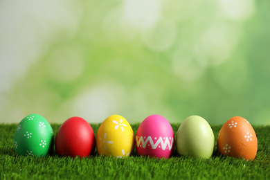 Photo of Colorful Easter eggs on green grass against blurred background. Space for text