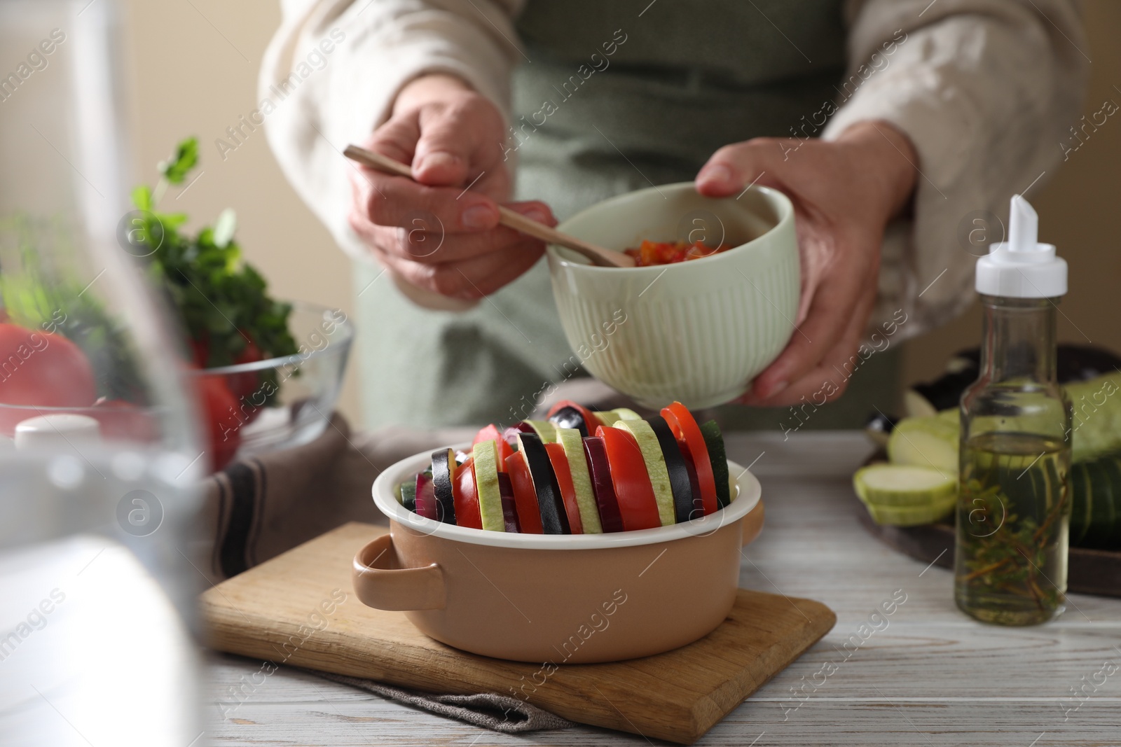 Photo of Cooking delicious ratatouille. Woman dressing fresh vegetables in bowl at white wooden table, closeup