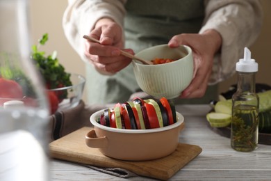 Cooking delicious ratatouille. Woman dressing fresh vegetables in bowl at white wooden table, closeup