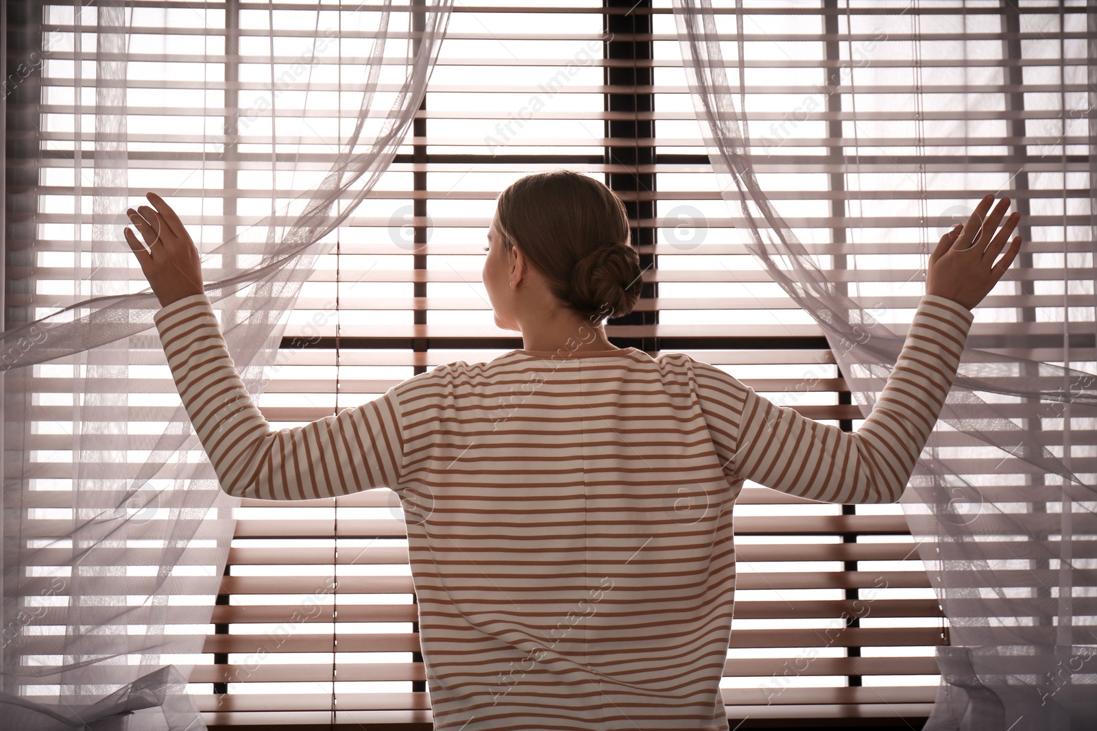 Photo of Woman opening window curtains at home in morning