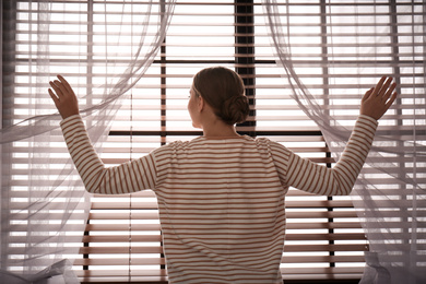 Woman opening window curtains at home in morning