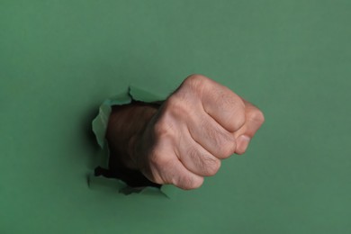 Photo of Man breaking through green paper with fist, closeup