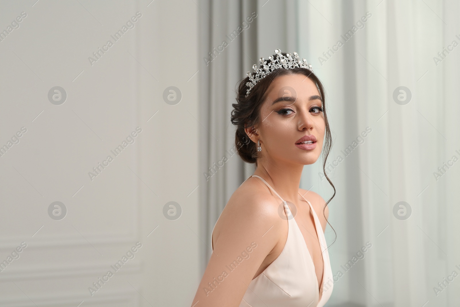 Photo of Beautiful young woman wearing luxurious tiara indoors, space for text