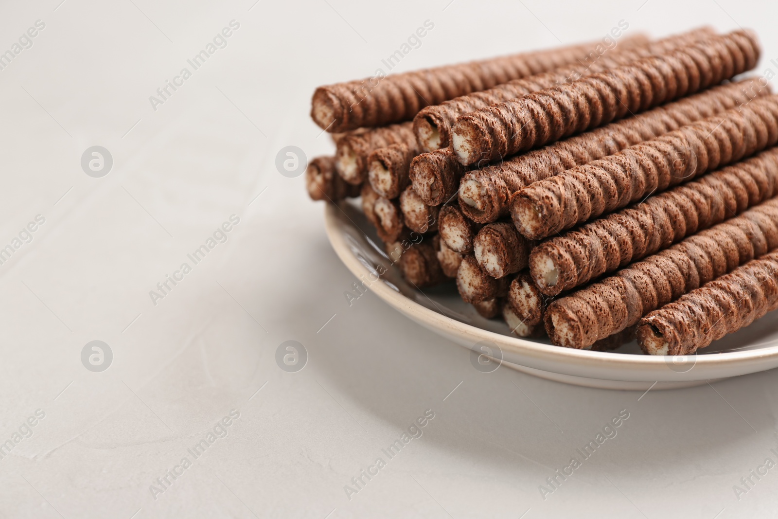 Photo of Plate with delicious chocolate wafer rolls on white table, space for text. Sweet food