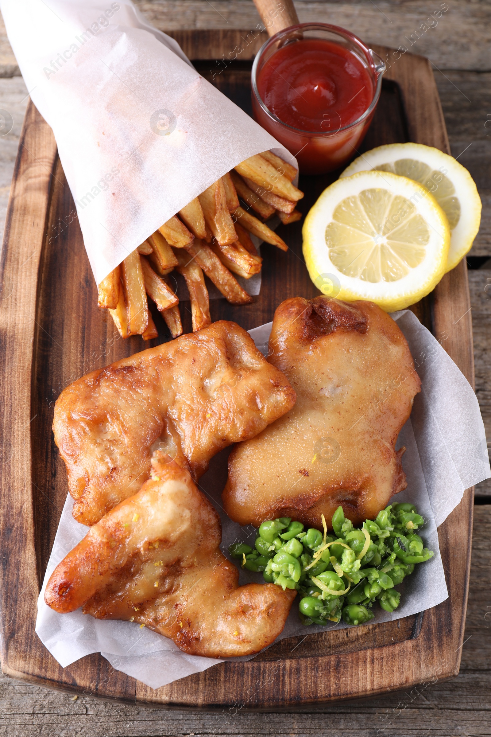 Photo of Tasty fish, chips, sauce and peas on wooden table, above view