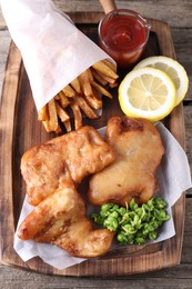 Photo of Tasty fish, chips, sauce and peas on wooden table, above view