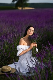 Beautiful young woman with bouquet sitting in lavender field