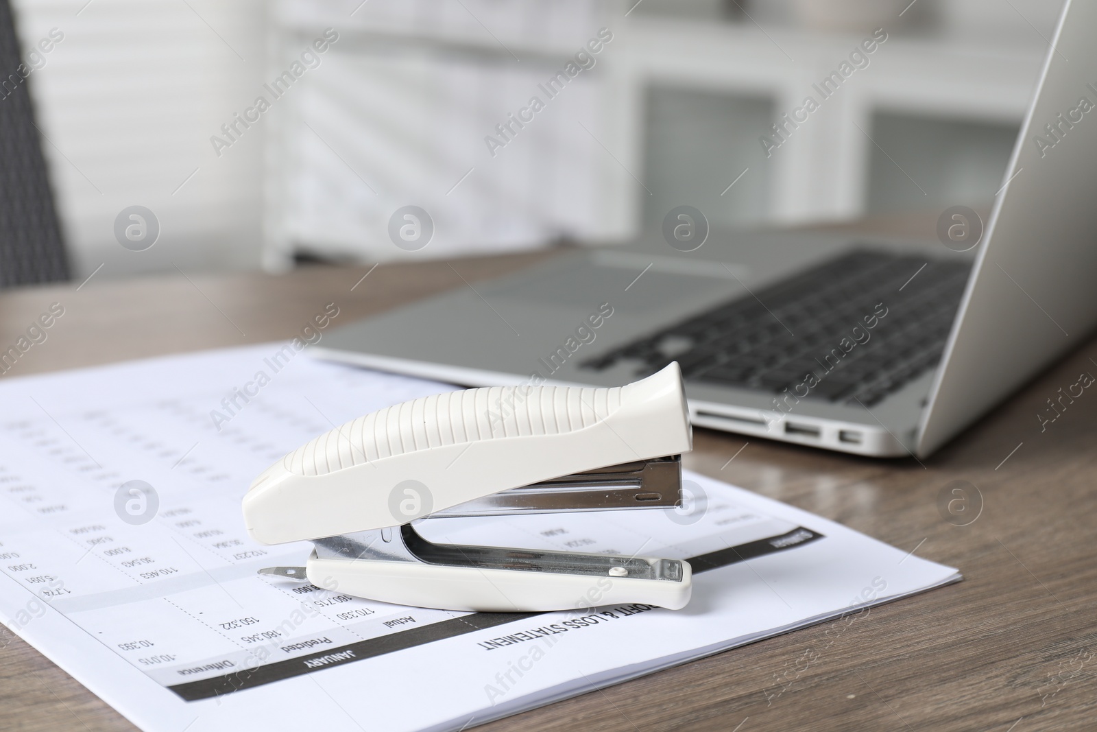 Photo of Stapler and document on wooden table indoors, closeup