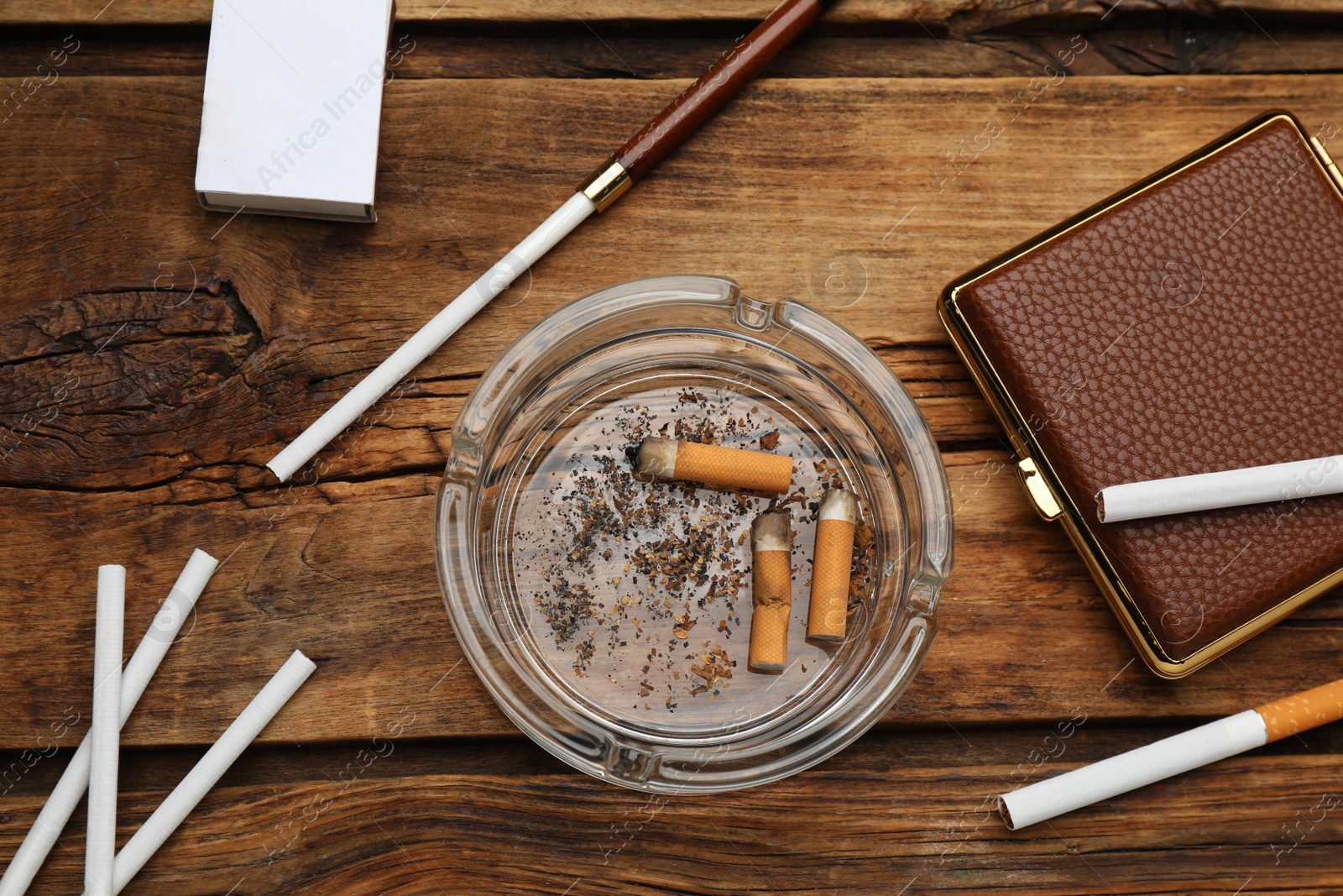 Photo of Cigarettes, case, holder, matchbox and ashtray with stubs on wooden table, flat lay