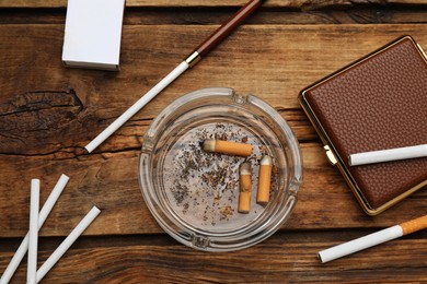 Cigarettes, case, holder, matchbox and ashtray with stubs on wooden table, flat lay